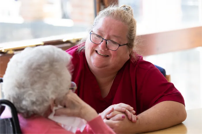 Smiling caregiver holding hands with an elderly woman in a wheelchair