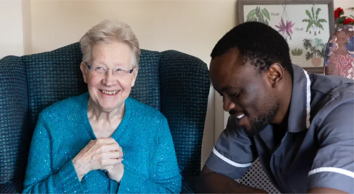 Elderly woman smiling beside a friendly male caregiver during an activity.