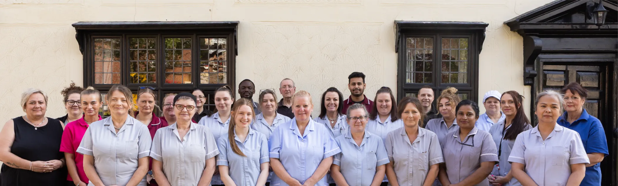 Group photo of care home staff standing outside in uniform, smiling at the camera.