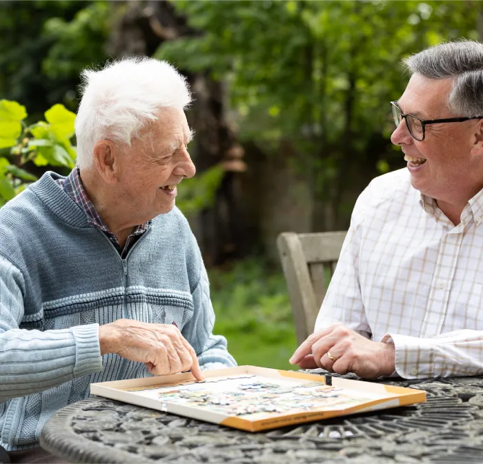 Two elderly men smiling and playing a board game outdoors